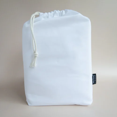 A white drawstring bag with a thick white cord, standing upright against a neutral beige background—perfect for storing your Little Human Linens waterproof sheet after use. A small black tag is attached to the side of the bag.