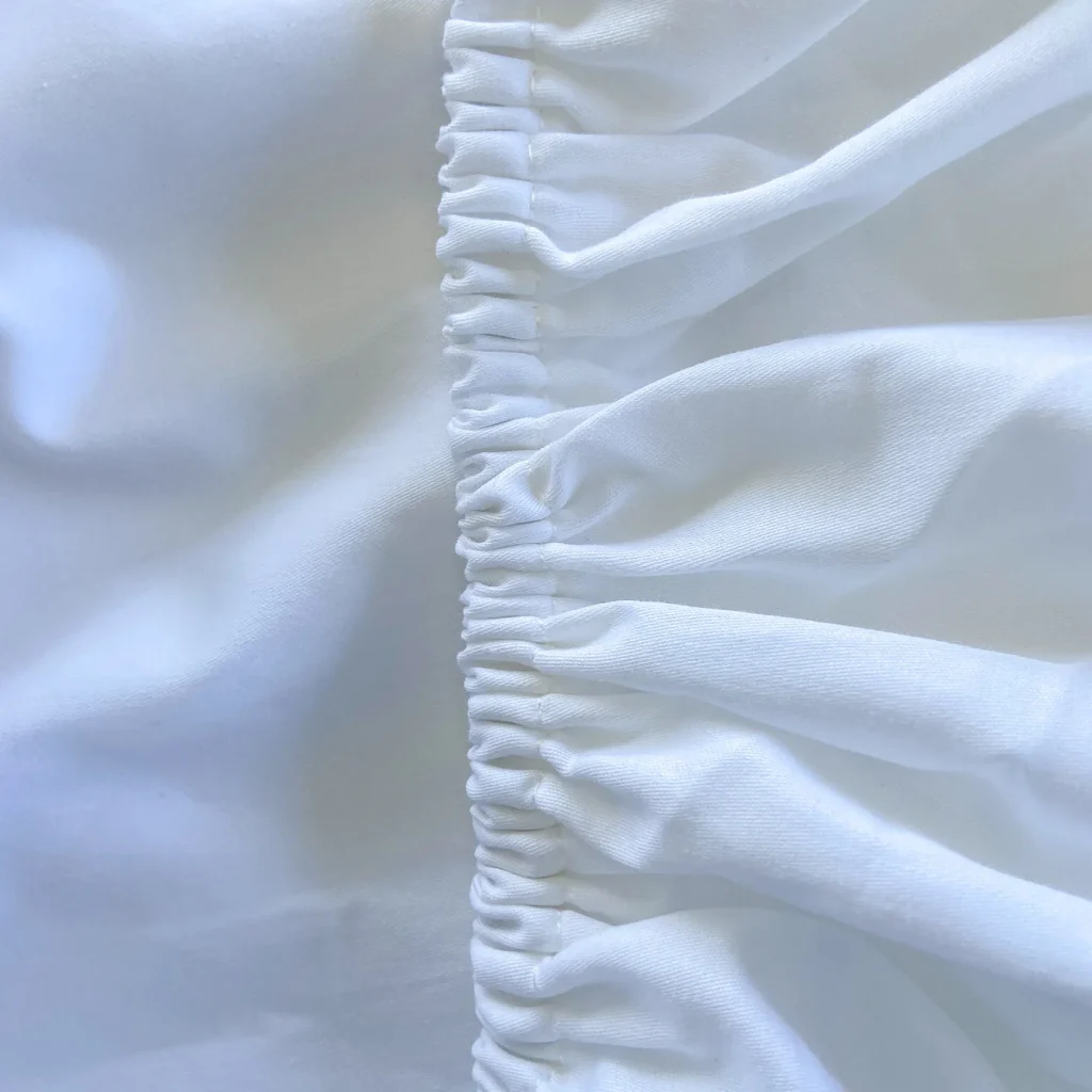 Close-up of white fabric with gathered, ruched stitching in the center—textured folds on the right, smoother surface on the left—similar to details noted in a Little Human Linens waterproof sheet review.