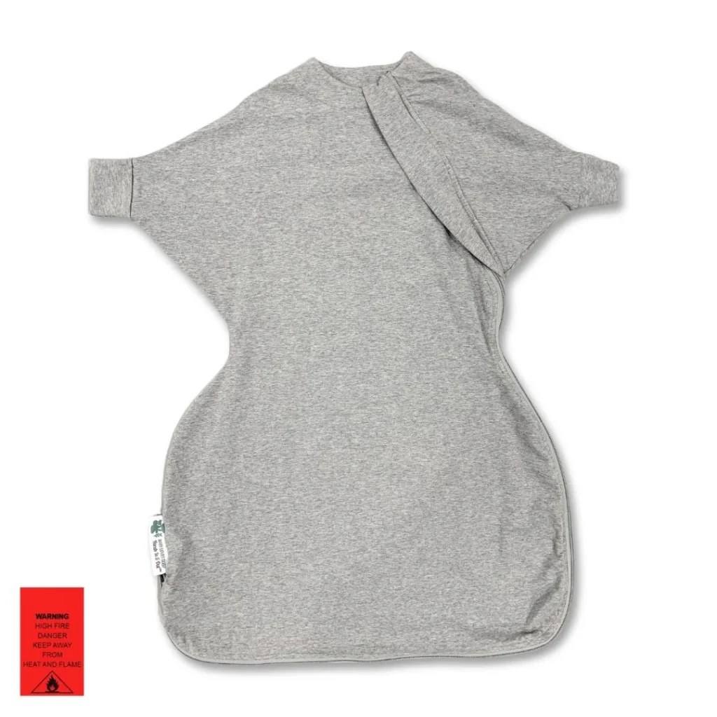 A gray Baby Loves Sleep Hands In & Out Sleep Sack is laid flat on a white background, featuring arm openings and a small red warning label in the lower left corner. The swaddle has a simple, streamlined design.