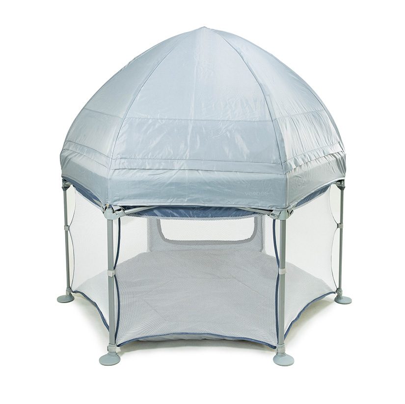 A portable, hexagonal playpen with mesh sides and a domed, light gray canopy cover, supported by six poles with round suction cup feet—ideal for infants or toddlers. Check out our KOOP Play Yard review for more details.