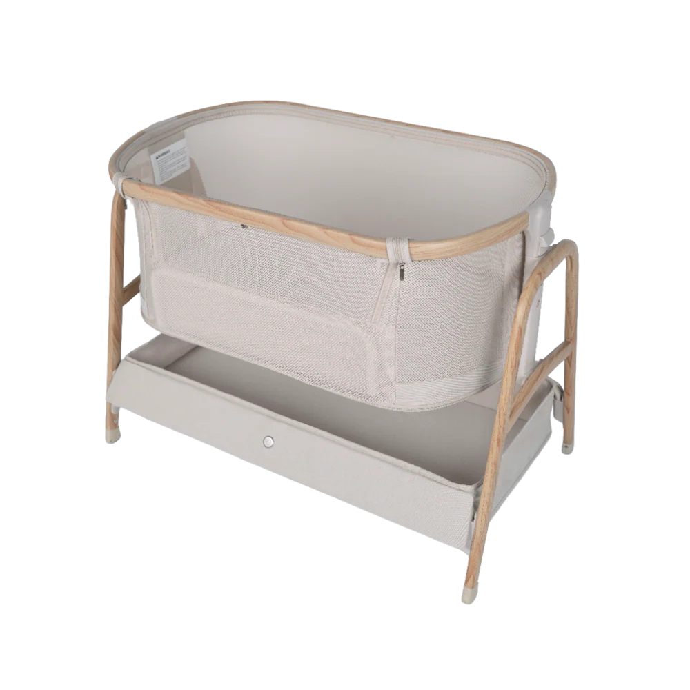 A beige Babybee Pod Bedside Sleeper with light wooden frame, mesh sides for breathability, and a rectangular storage shelf underneath. The design is modern and minimalist—perfect for any nursery.